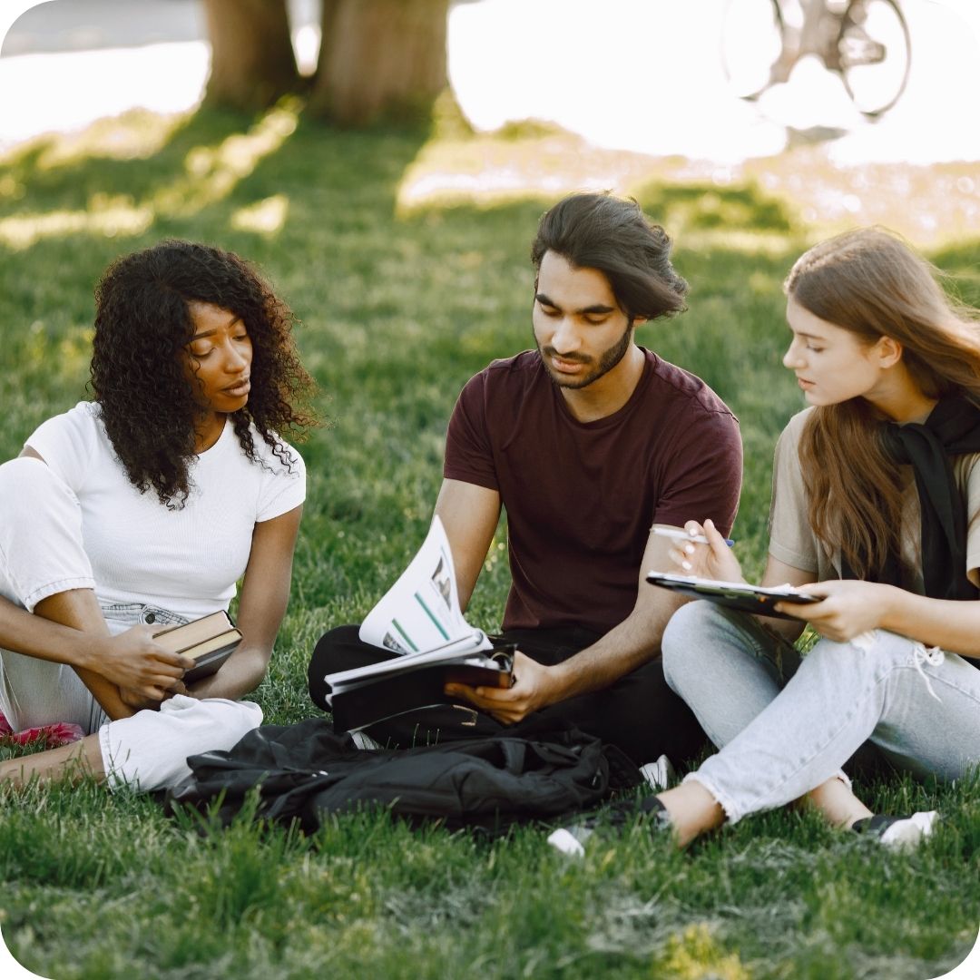 Three International students studying together on a grassy lawn.