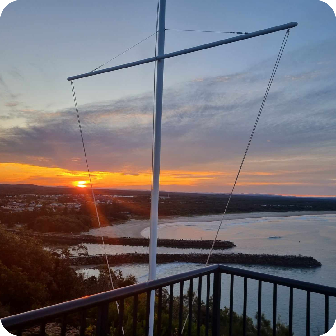 A sunset over a body of water from a balcony with a flagpole at the Evans Head Campus